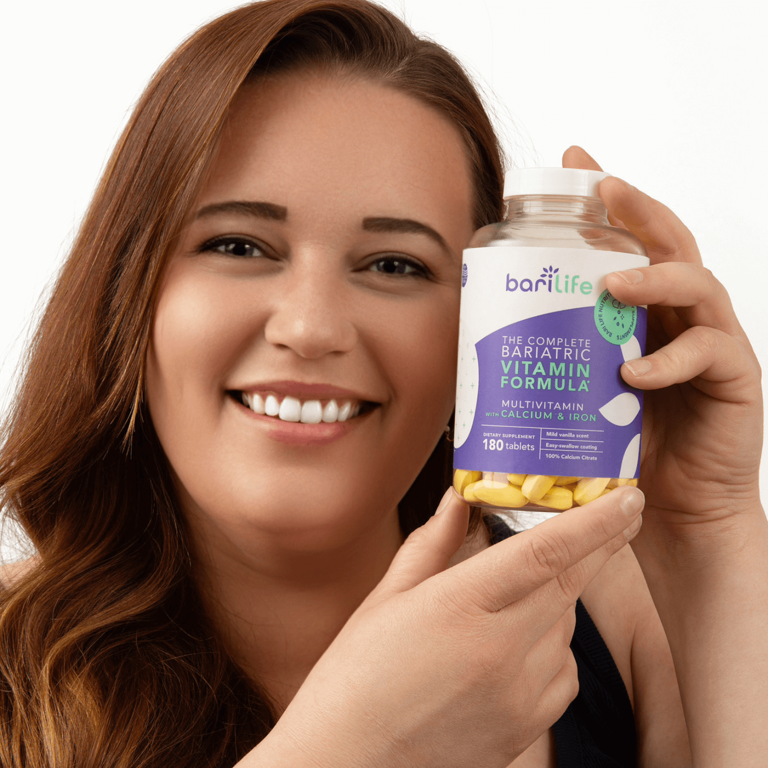 Woman holding a bottle of Complete Bariatric Vitamin Formula, showcasing multivitamins with calcium and iron.
